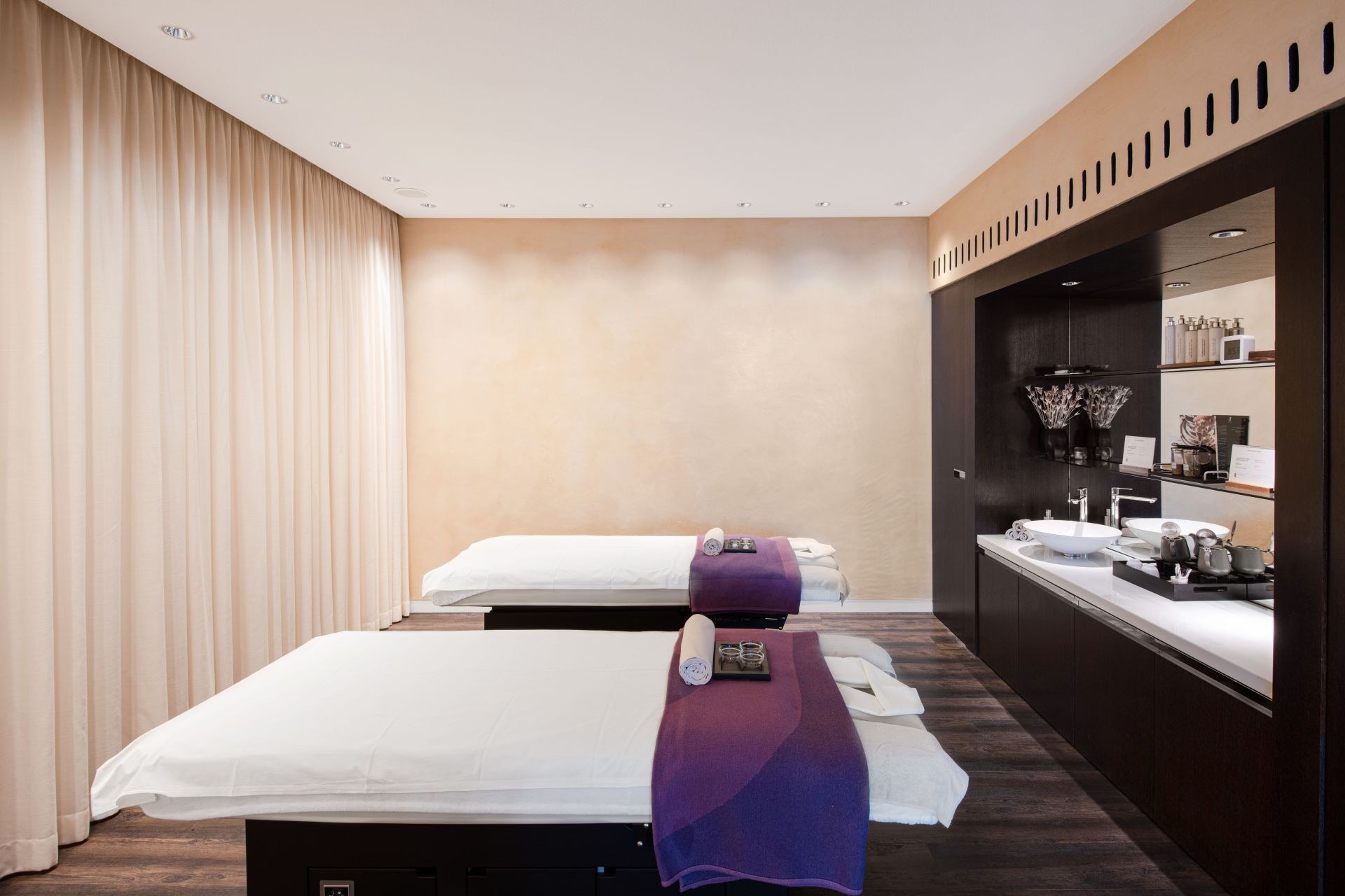 A treatment room for two at The Dolder Grand Spa, with curtains, warm light and a dark wood washstand